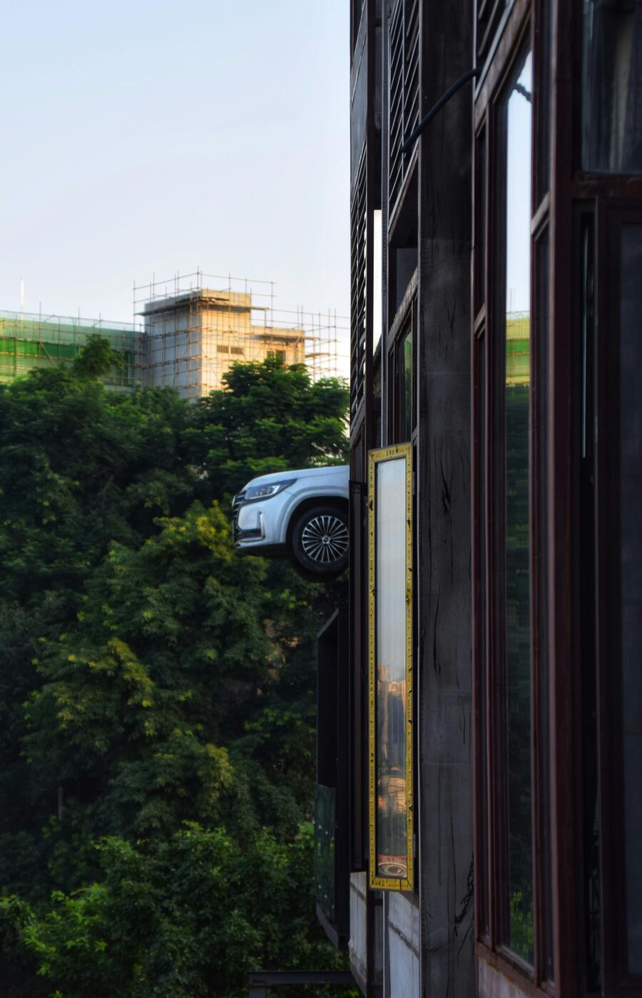 Selbst Schaufenster trotzen der Schwerkraft. Diese Installation an der Fassade eines Gebäudes verwandelt ein schwebendes Auto in ein urbanes Kunstwerk, in einer Stadt, in der das Unmögliche alltäglich erscheint. Foto: Chenyu Guan. Foto: Chenyu Guan. Chongqing. China.